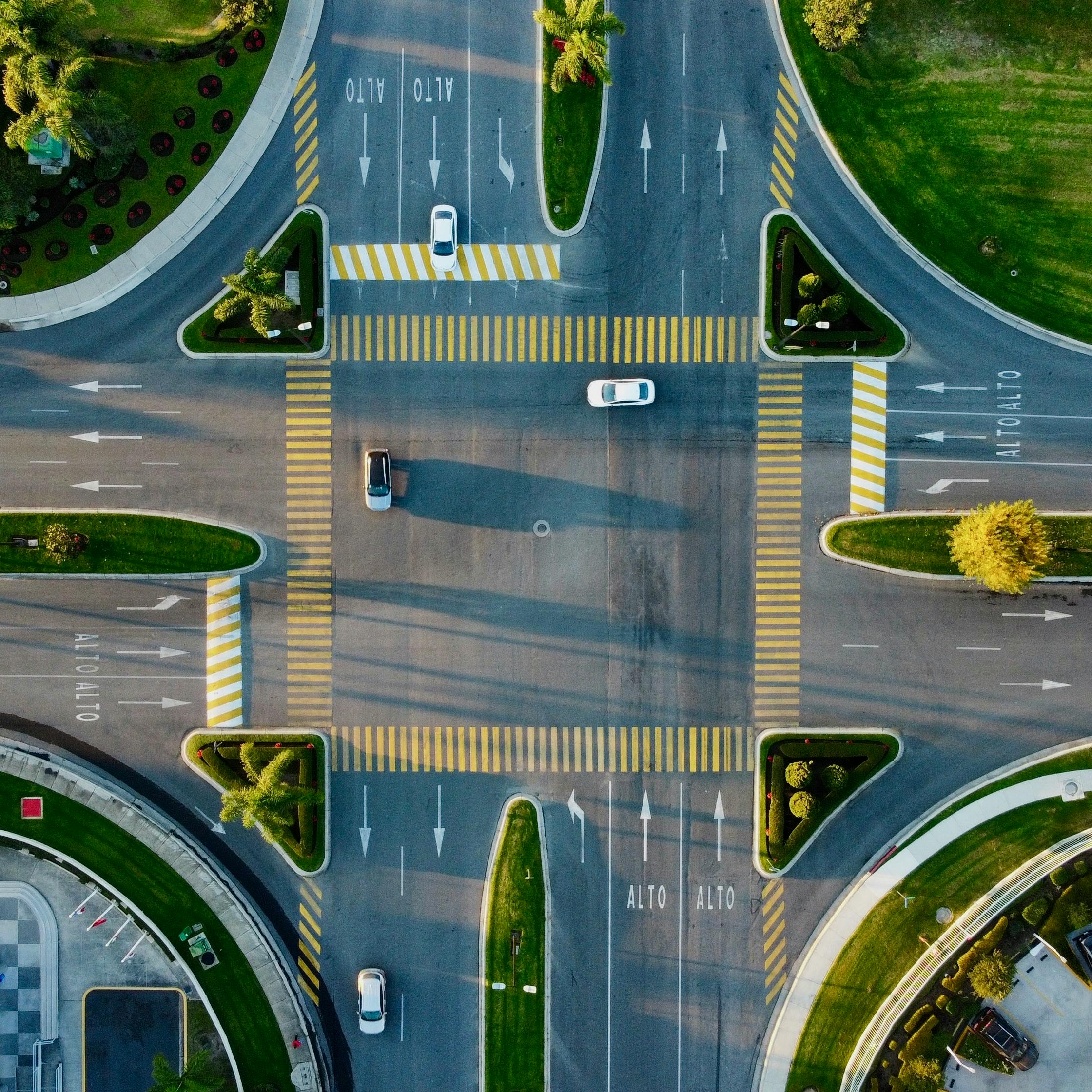 Top-down aerial shot of a city intersection with cars and green landscapes.